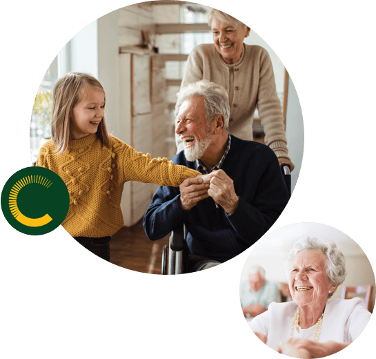 A little girl holding the hand of an older man in a wheelchair with an older woman pushing from behind, all are smiling and an older woman smiling